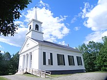 église blanche avec un haut clocher et des piliers à l'avant.