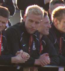 Blond Andrew Davies, leaning on a railing in a crowd