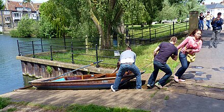 A punt being pulled up rollers on the slipway between the upper and lower levels of the River Cam near the Mill Pool.