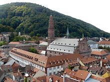 Vue des toits, le collège est un grand bâtiment en L, l'église baroque est en grès rose. À l'arrière plan, des collines boisées.