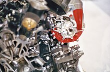 Cutaway H2R engine and supercharger. Orange painted plenum surrounds impeller, behind which is visible part of planetary gear system. Kawasaki Ninja H2R engine cutaway supercharger.JPG