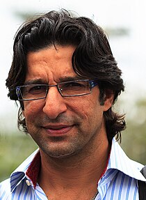 A man in a pale blue and white shirt, near-shoulder length hair, wearing rectangular-framed glasses