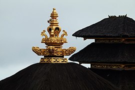 A gold-colored roof pinnacle and thatched roof made of black ijuk fibers.