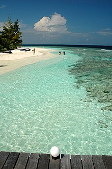 L'isola-resort di Bathala, ripresa da un pontile. A destra della spiaggia è chiaramente visibile la barriera corallina, in questo caso vicinissima alla battigia.