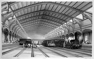 Dos trenes y dos vías vacías debajo de un techo ornamentado, que se aleja en la distancia.