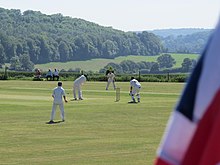A Union Flag in the foreground and a cricket match with English countryside in the background