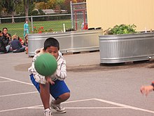 A boy crouching with a green utility ball speeding toward him