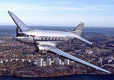 An aircraft in flight with city buildings in background