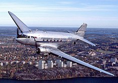 Ein Flugzeug im Flug mit Stadtgebäuden im Hintergrund