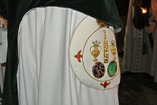 Escudo de la Hermandad de la Macarena de Madrid en la capa de un nazareno que se encuentra en la calle, parado y procesionando