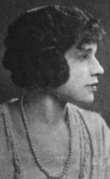 A Black woman with light skin, photographed in profile, her hair dressed over her ears with curly bangs