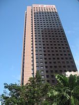 Ground-level view of a 30-storey, box-like structure with a square cross section. The corner is windowless and slightly receded from the rest of the structure.