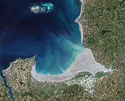 Image satellite de la baie du Mont-Saint-MichelCette image satellite permet d'observer deux paysages différents correspondant à deux grands ensembles morpho-sédimentaires : le domaine occidental, de Cancale à Cherrueix, correspond à un fond de baie abrité. Cet estran large de 5 km, à pente modérée (de 3 à 10 ‰), comprend des vases entaillées par les « biez » (terme local désignant les canaux de drainage du marais de Dol. Le domaine oriental, de Cherrueix à la pointe de Champeaux, correspond à un complexe estuarien au débouché de trois petits fleuves côtiers (la Sée, la Sélune et le Couesnon). Cet estran large de 10 km, très plat, est parcouru par des chenaux  de rivière à tendance méandriforme, et un réseau dense de chenaux de marée aux tracés plus rectilignes..