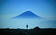 テントを担いで南アルプスを縦走する登山者、間ノ岳山頂部、遠景は富士山。