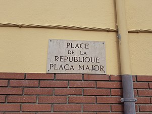 Placa bilingüe a la plaça Major d'Elna.