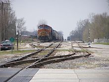 A CSX freight train with run-through BNSF power waits for yard clearance in Monon, Indiana. Rail line from west (CLight).jpg