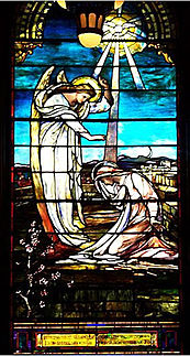 A Virgem Maria se ajoelha para receber a mensagem de Deus de um anjo.  A pomba do Espírito Santo desce em raios de luz.