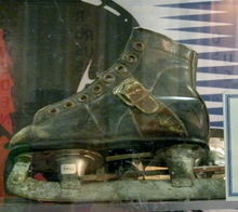 A small pair of ice skates, meant for a small child. The boot is leather and is missing its laces, while the blade is deteriorating and showing significant wear due to age.