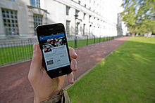 Photograph of person's left hand holding a smartphone that is accessing social media