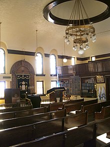 The sanctuary as seen from the North corner, with the Torah ark at the left, the reader's desk in the center, and the women's balcony at the upper right. As originally built, the bimah was centered below the chandelier. B'NaiJacobOttumwaInteriorFromNorth.jpg