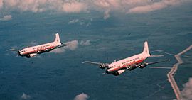 Two airplanes flying side-by-side over green fields