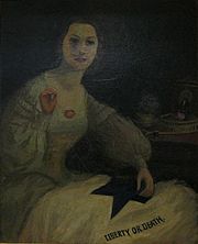 Portrait of an attractive young woman in mid-19th century dress sewing a flag that says "Liberty or Death"