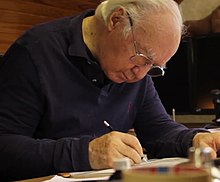 Photographie d'un dessinateur appliqué sur son dessin, portant des lunettes.