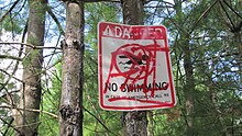 Vandalized "Danger, No Swimming" sign posted near the water-filled excavation pit Sharpner's Pond "No Swimming" Sign.jpg
