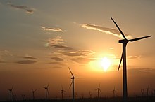 Photograph of wind turbines against a hazy orange sky