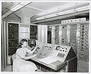 Technician inspecting film at FOSDIC console. A paper input form is on the desk. Woman inspecting FOSDIC film.jpg