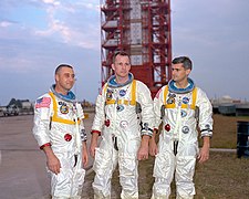 Fotografia a colori dell'equipaggio dell'Apollo 1 in posa davanti alla stazione di tiro in tuta.