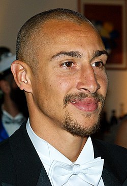 The head and shoulders of a man in his 30's, wearing a black blazer and white box tie