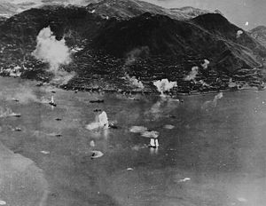 Въздушна снимка на остров с градска зона по брега и стръмна планина в центъра. Много кораби са до острова, а в близост до някои от тях изригват струи вода.