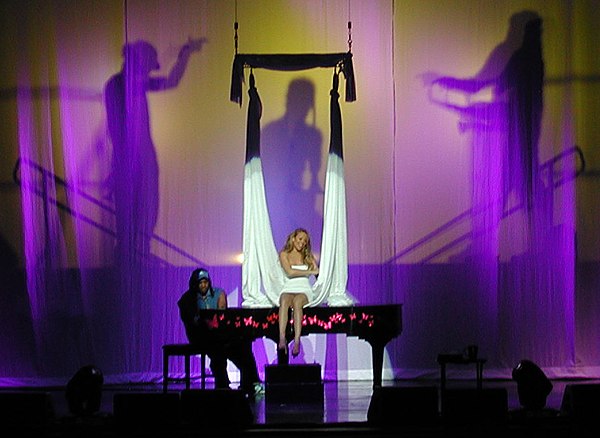 Carey performing "Subtle Invitation", seated on top of a piano, on the Charmbracelet World Tour (2003–04)