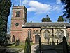 A church with a brick Neoclassical tower and body and a stone Gothic chapel protruding in the foreground