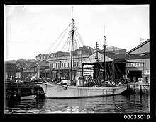 Sam Hood 1923 photograph of the sailing ketch Corwa berthed near the Union Steam Ship Company of New Zealand's wharf in Darling Harbour. The Grafton Bond Store can be seen top left. Sailing ketch CORWA berthed alongside a wharf in Darling Harbour, Sydney (8638121445).jpg