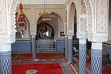 Nebenraum im Mausoleum von Sidi Abdallah Ibn Hassun mit zwei von der Decke hängenden Wachslaternen. Im Hintergrund sein Kenotaph (arabisch tābūt)