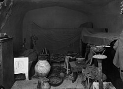 Plain-walled room densely packed with neatly arranged furniture and offerings