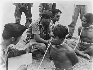 Two men with rope around their necks are handcuffed by TNI officers in September 1948 in Madiun, Indonesia Twee mannen met touw geboeid worden ondervraagd door TNI-officieren, Bestanddeelnr 8812.jpg