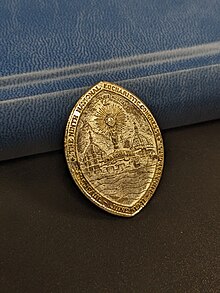 A commemorative pin from the 1941 Eucharistic Congress. Depicted are the Cathedral of Saint Paul and the Basilica of Saint Mary, in between them the Tissot monstrance. Surrounding is the text "THE NINTH NATIONAL EUCHARISTIC CONGRESS. SAINT PAUL JUNE 1941 MINNEAPOLIS"