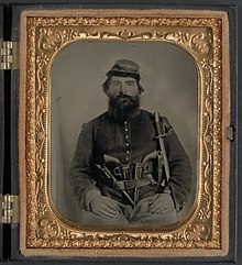 Union cavalryman A.J. Blue armed with three pistols and a sword. A. J. Blue, cavalry soldier in Union shell jacket and bummer cap with three Remington revolvers in his belt, holding a sword LCCN2011645425.jpg