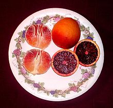 A plate showing three blood oranges: one whole, one peeled, and one sliced in half