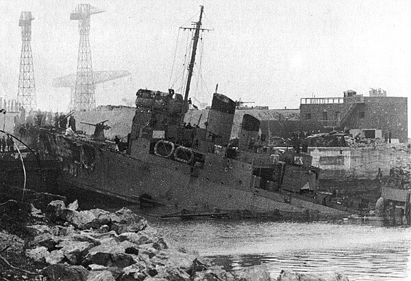 HMS Campbeltown wedged in the dock gates. Note the exposed forward gun position on Campbeltown and the German anti-aircraft gun position on the roof o