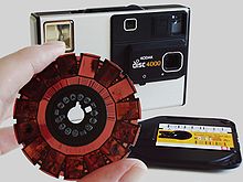 Kodak disc film negative (with camera and film cartridge in background) Camera Kodak Disc 4000 with disc film.jpg