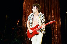 Zdjęcie mężczyzny grającego na jaskrawoczerwonej gitarze w rozpiętej koszuli i nagim torsie