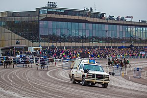 Lähtöauto, sen taakse kerääntyviä hevosia, yleisöä ja Vermon katsomorakennus