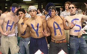 Five young shirtless men pose defiantly in a crowd. Each has a letter in blue on their chests to spell HOYAS.