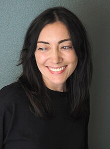 A photograph of Kerry Howley depicting her head and shoulders. She is wearing a black sweater, smiling broadly, and looking sideways.