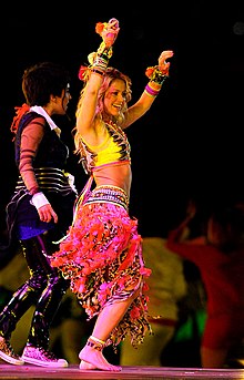 Shakira onstage, singing and playing guitar