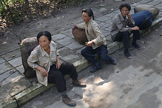 A group of aged women with full backpacks sitting on the street.
